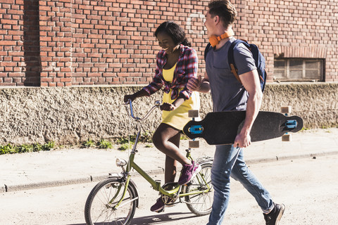 Junges Paar mit Fahrrad und Skateboard zu Fuß auf der Straße, lizenzfreies Stockfoto