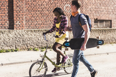 Young couple with bicycle and skateboard walking in the street - UUF10558