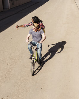 Young man riding bicycle with his girlfriend standing on rack, taking selfies - UUF10561