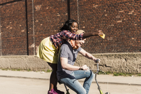 Young couple riding bicycle in the street, woman standing on rack, taking selfies stock photo