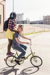 Young couple riding bicycle with girl standing on rack - UUF10565