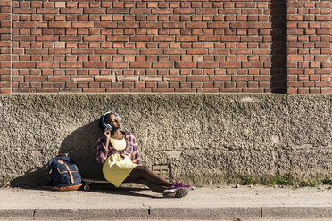 Junge Frau sitzt auf dem Boden und hört Musik mit Kopfhörern - UUF10570