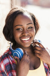 Porträt einer glücklichen jungen Frau mit Kopfhörern um den Hals - UUF10571