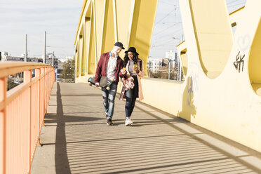 Young couple with skateboard walking on bridge - UUF10576