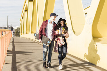 Young couple with skateboard walking on bridge - UUF10577