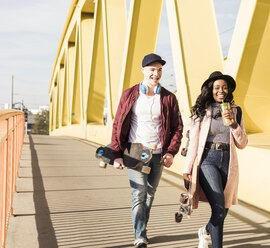 Young couple with skateboard walking on bridge - UUF10578