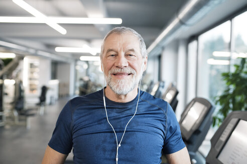 Portrait of fit senior man with earphones in gym - HAPF01649