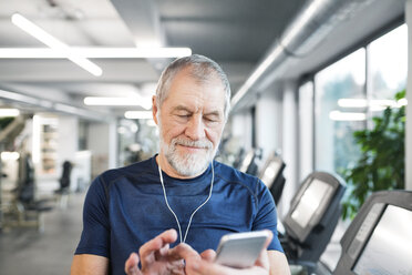 Älterer Mann mit Smartphone und Kopfhörern im Fitnessstudio - HAPF01650