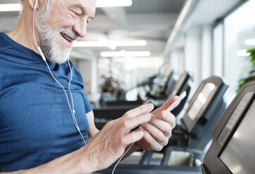 Älterer Mann mit Smartphone und Kopfhörern im Fitnessstudio - HAPF01653