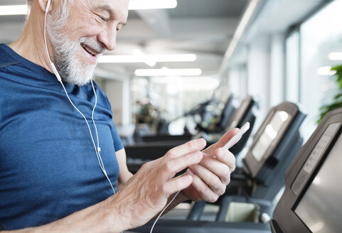 Senior man with smartphone and earphones in gym - HAPF01653