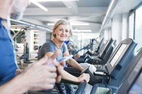 Gruppe von fitten Senioren auf Laufbändern im Fitnessstudio, Frau lächelt - HAPF01654