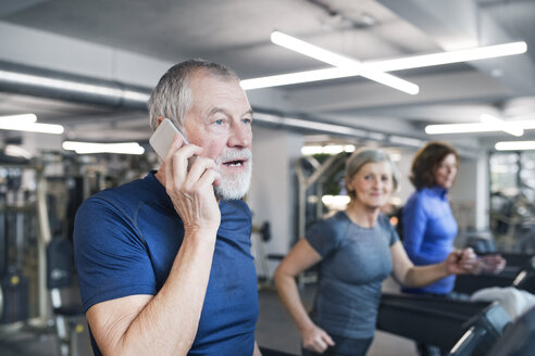 Group of fit seniors working out on treadmills in gym, man with smart phone - HAPF01656