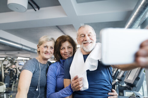 Group of fit seniors in gym taking a selfie with smartphone after working out - HAPF01662