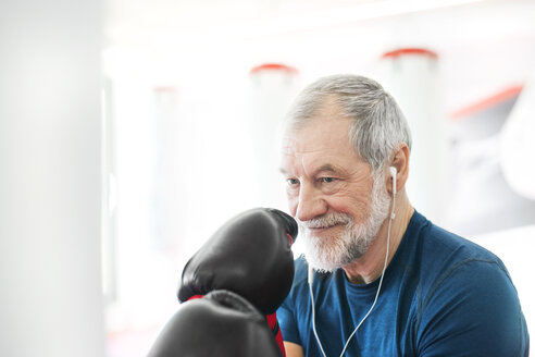 Fit senior man with earphones and boxing gloves in gym - HAPF01670