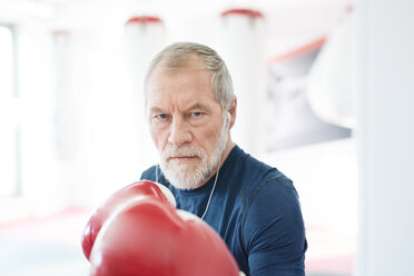Porträt eines ernsten älteren Mannes mit Kopfhörern und Boxhandschuhen im Fitnessstudio - HAPF01672