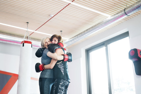 Zwei glückliche ältere Frauen mit Boxhandschuhen umarmen sich im Fitnessstudio, lizenzfreies Stockfoto