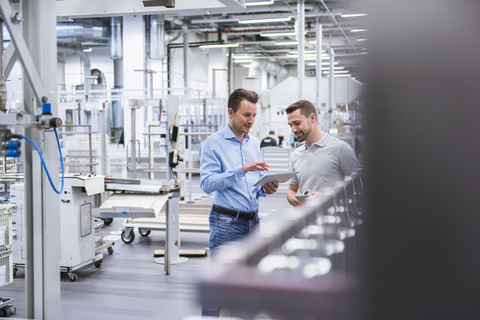 Zwei Männer mit Tablet im Gespräch in einer Fabrikhalle, lizenzfreies Stockfoto