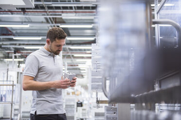 Mann mit Tablet in einer Fabrikhalle, der Produkte untersucht - DIGF02345