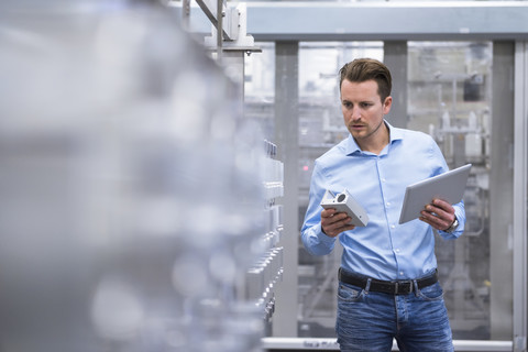 Mann mit Tablet in einer Fabrikhalle, der Produkte untersucht, lizenzfreies Stockfoto