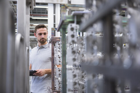 Mann mit Tablet in einer Fabrikhalle, der Produkte untersucht - DIGF02354