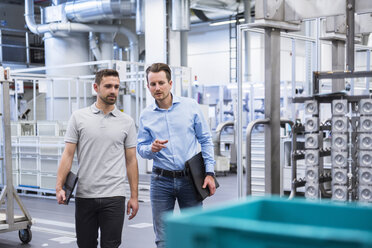 Two men walking and talking in factory shop floor - DIGF02362