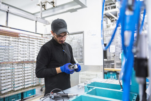 Mann arbeitet in einer Fabrikhalle und betrachtet ein Produkt - DIGF02366