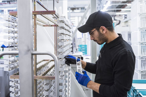 Man working in factory shop floor hanging products on rack - DIGF02367