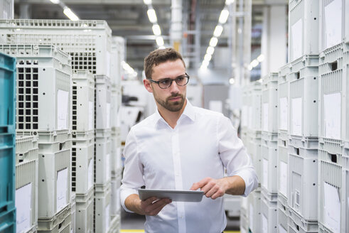 Man using tablet at boxes in factory shop floor - DIGF02374