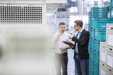 Two men with tablet talking at boxes in factory shop floor - DIGF02379