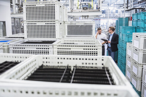 Two men with tablet talking at boxes in factory shop floor - DIGF02380