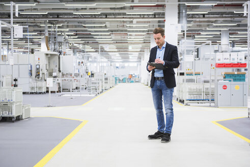 Man standing in factory shop floor taking notes - DIGF02384