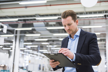 Man standing in factory shop floor taking notes - DIGF02385