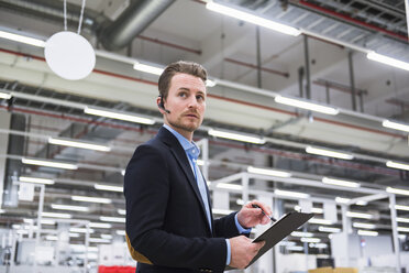 Mann mit Headset in einer Fabrikhalle macht sich Notizen - DIGF02386