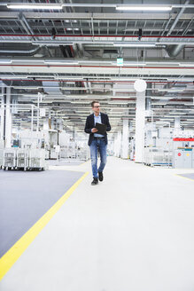 Man walking in factory shop floor taking notes - DIGF02389