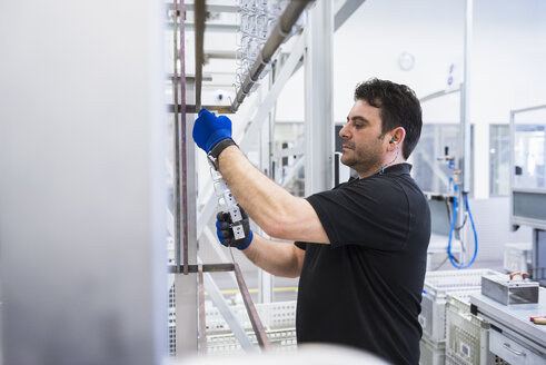 Man working in factory shop floor hanging products on rack - DIGF02394