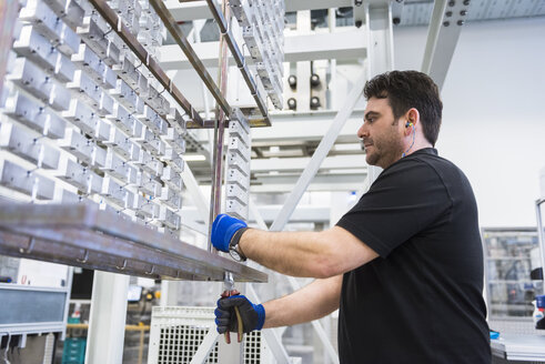 Man working in factory shop floor hanging products on rack - DIGF02395