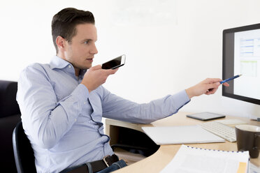 Businessman with smartphone looking at computer screen - FMOF00241