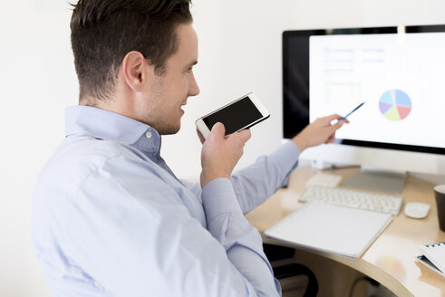 Geschäftsmann mit Smartphone, der ein Tortendiagramm auf einem Computerbildschirm analysiert - FMOF00242