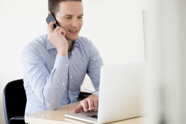 Smiling businessman on the phone using laptop - FMOF00243