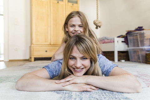 Porträt eines lächelnden kleinen Mädchens, das auf dem Rücken seiner Mutter auf dem Boden liegt, lizenzfreies Stockfoto