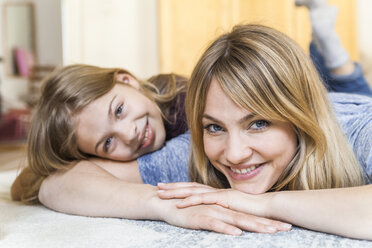 Porträt einer lächelnden blonden Frau, die mit ihrer Tochter auf dem Boden liegt - TCF05396