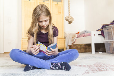 Mädchen sitzt auf dem Boden eines Kinderzimmers und liest ein Buch - TCF05397