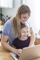 Mother and daughter using laptop in kitchen - TCF05398