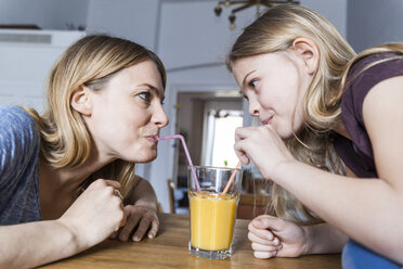 Mother and daughter sharing an orange juice in kitchen - TCF05400
