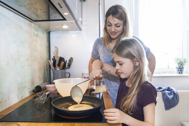 Mother and daughter baking pancakes in kitchen - TCF05403