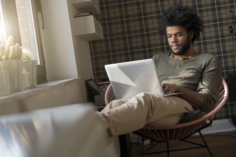 Mann sitzt im Wohnzimmer im Sessel und arbeitet am Laptop, lizenzfreies Stockfoto