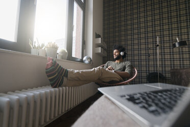 Man sitting in living room in armchair listening to music - SBOF00385