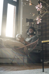 Man sitting in living room in armchair holding mirror ball listening to music - SBOF00387