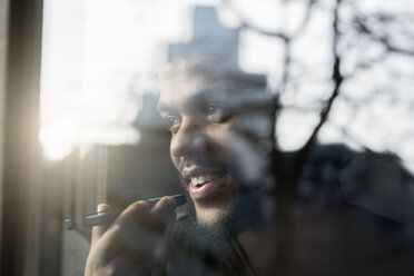 Man at window looking outside talking into smartphone - SBOF00390