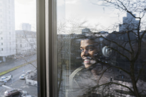 Mann am Fenster, der nach draußen schaut und mit Kopfhörern Musik hört, lizenzfreies Stockfoto